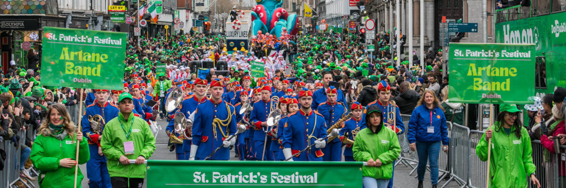 St. Patrick’s Day parade in Dublin featuring the Artane Band marching down a crowded street with vibrant green decorations and festive floats, near The Grafton Hotel